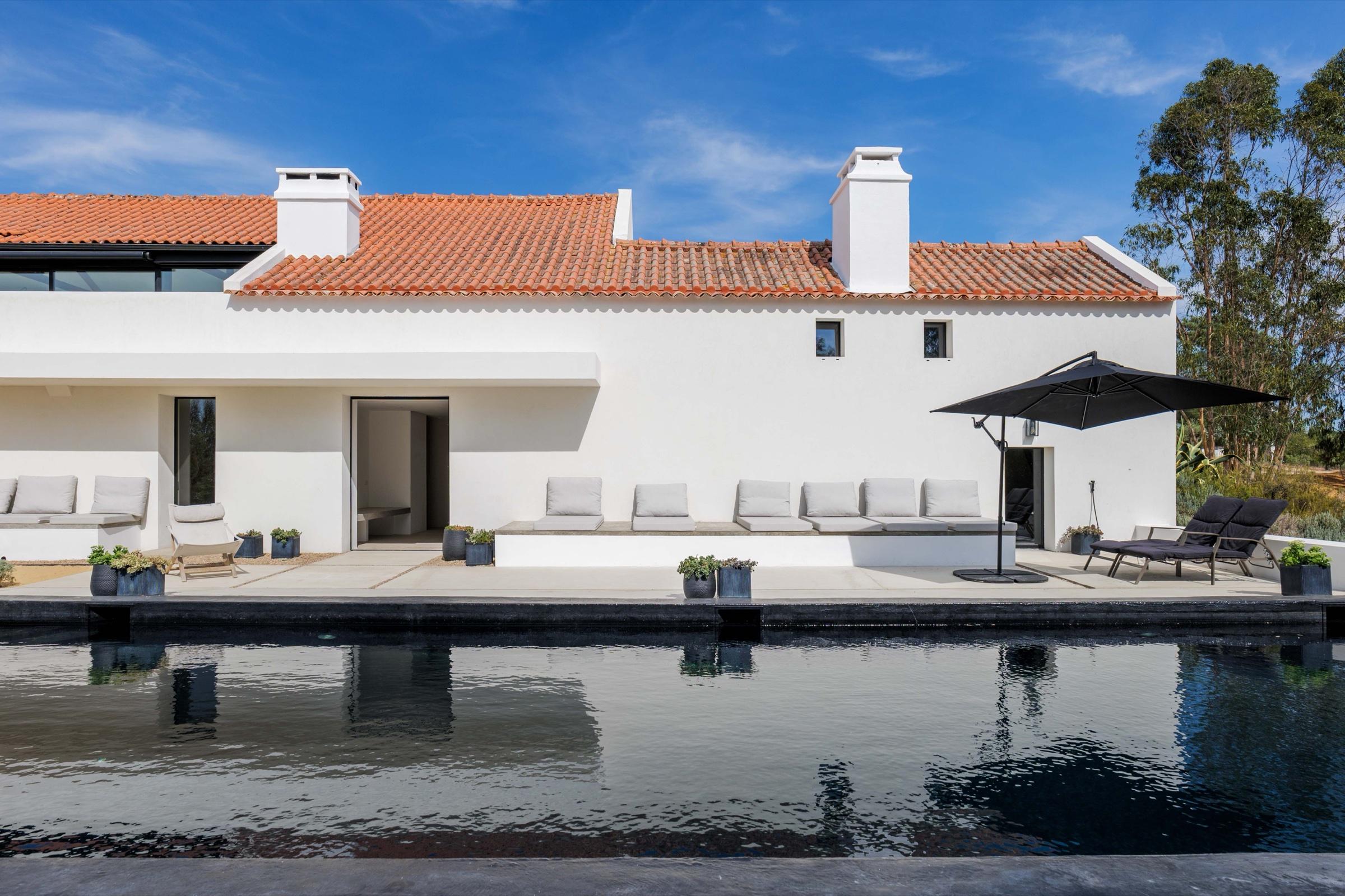 The whitewashed Portugal retreat house with its terracotta roof, lounge seating, and black reflecting pool